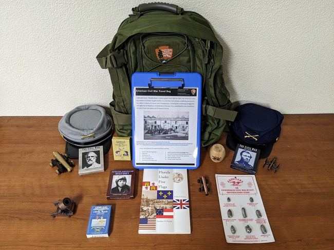 A green NPS backpack with hands-on materials and a book.